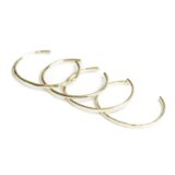 Four thin gold bangles set out on a white background.