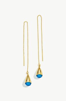 Two gold earrings with long chain tops and droplet shaped blue bottoms laid out on a white background.
