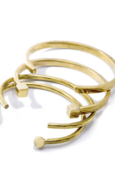 Four cuff-style gold bracelets on a white background with various shaped ends.