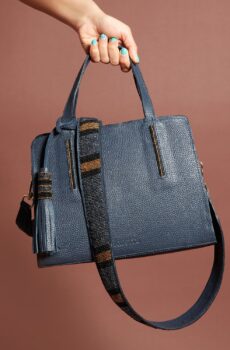 A navy blue bag with a navy, black, and brown beaded strap and tassel. A hand with blue-green nail polish is holding the bag from above.