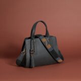 A black leather bag with a beaded strap and tassel.
