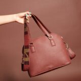 A dark red leather handbag with a zippered top, handles and a beaded brown, black, and red shoulder strap.