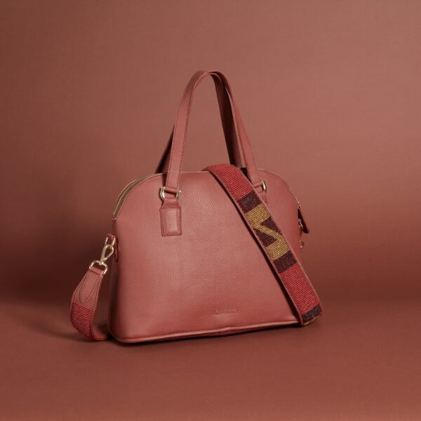 A dark red leather handbag with a zippered top, handles and a beaded brown, black, and red shoulder strap.