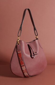 A maroon saddlebag-style purse with a short strap, a drawstring, and a red and brown beaded shoulder strap