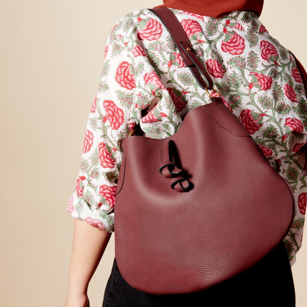 A person wearing a floral shirt with a dark red leather bag slung over their left shoulder.