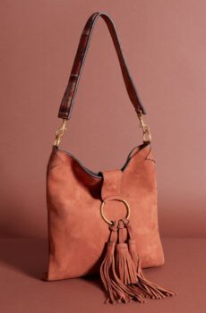 A warm cognag colored shoulder bag with a long shoulder strap and a large tassel attached to a metal ring on the closure