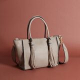 a cool greyish-brown leather bag with handles, a strap, and two tassels