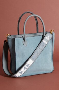 A blue-grey leather tote-style bag with handles and a long grey and white beaded shoulder strap